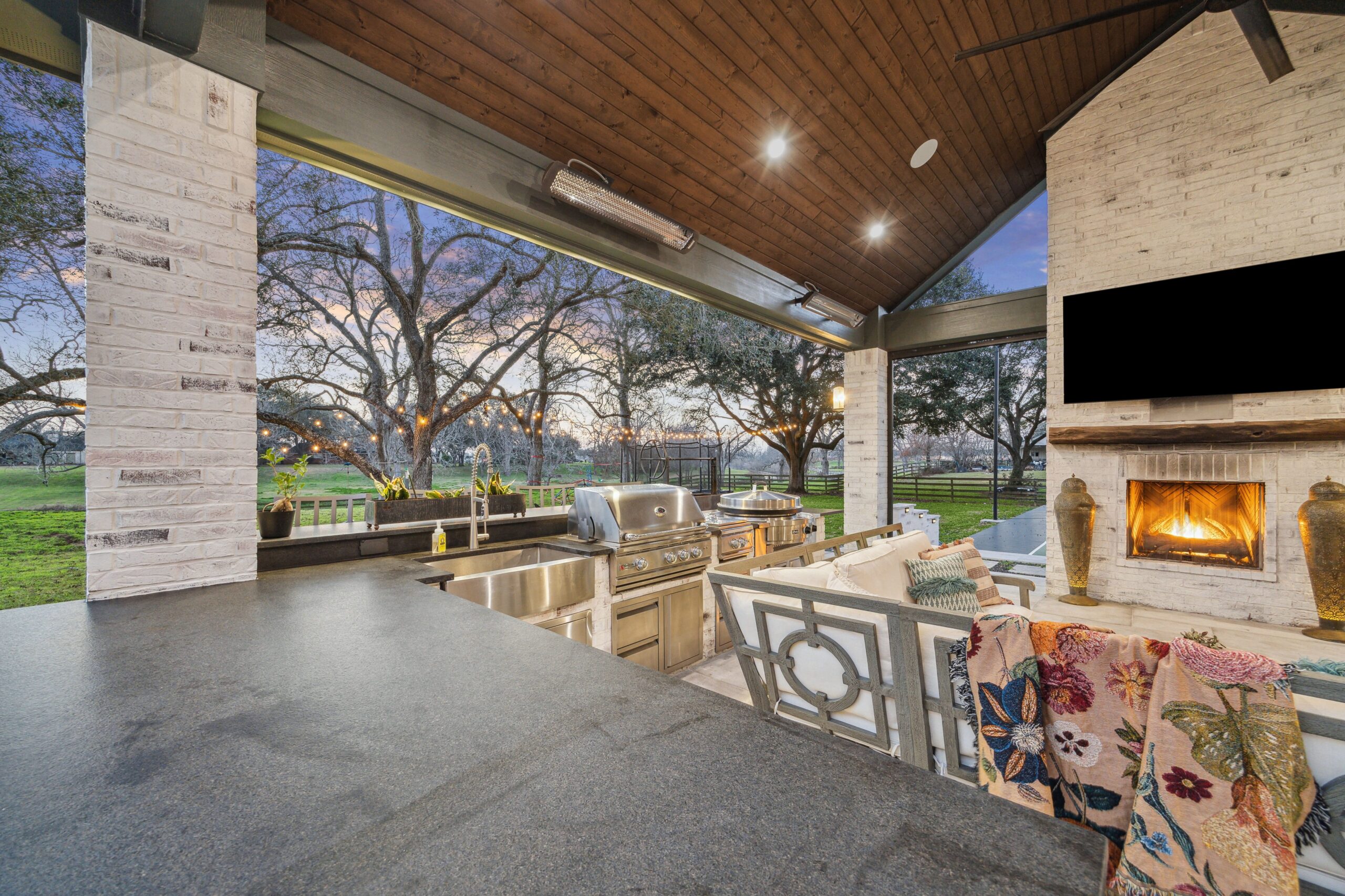 A beautifully designed outdoor living space featuring a covered patio, outdoor kitchen, gas fireplace, and sport court, perfect for entertaining in Houston.