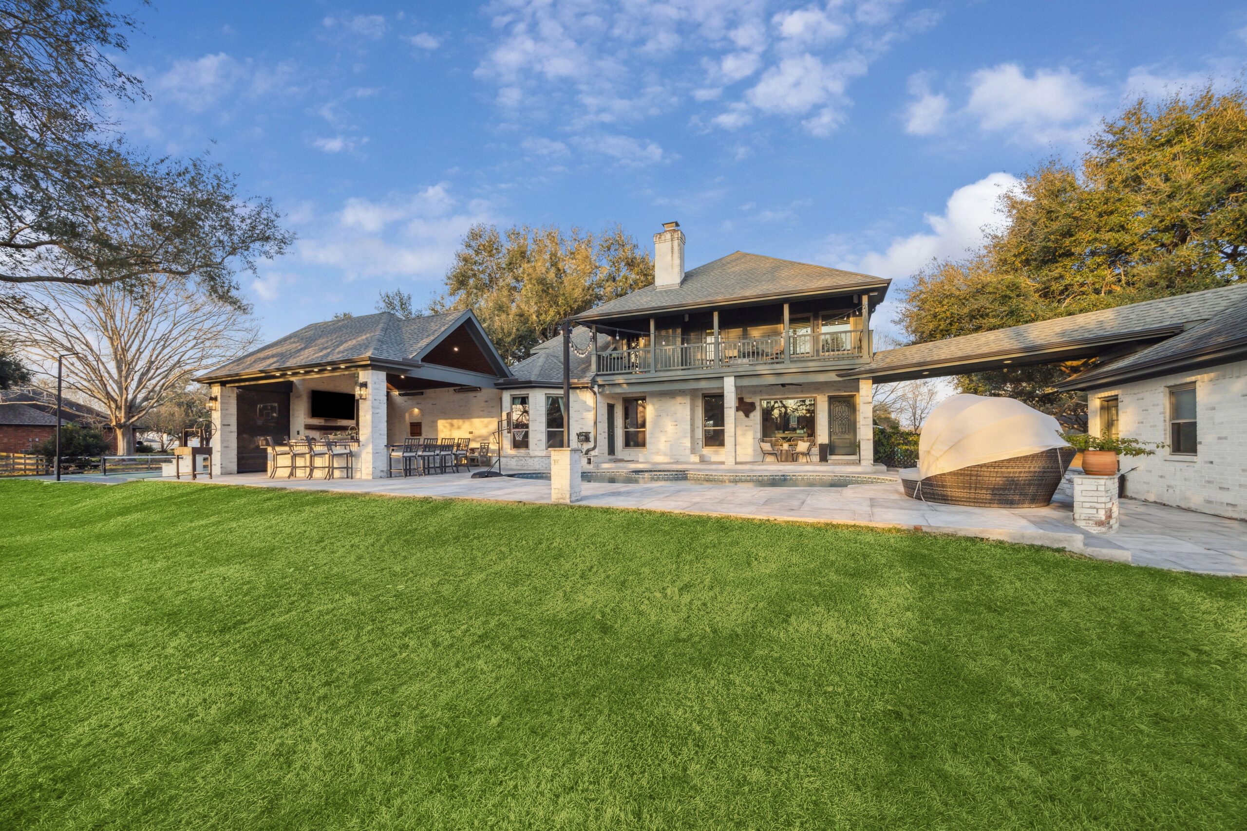 A beautifully designed outdoor living space featuring a covered patio, outdoor kitchen, gas fireplace, and sport court, perfect for entertaining in Houston.